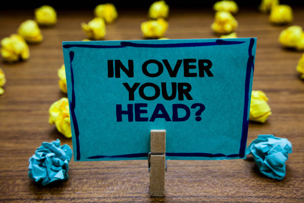 istock Handwriting text In Over Your Head question. Concept meaning To be involved in a difficult situation problem Blurry wooden deck yellow and blue lob on ground paper clip grip page with text. 1063948184