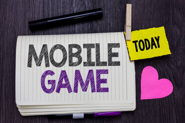istock Text sign showing Mobile Game. Conceptual photo they are entertaining programs made to work on smart device Open notebook clothespin holding reminder marker heart wooden background. 1063948248