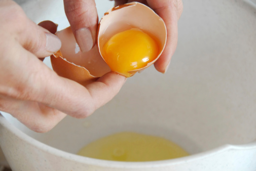 broken egg in hands with separated yolk closeup