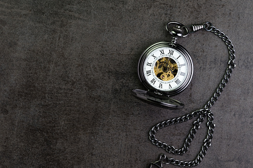 Vintage retro pocket watch on dark black chalkboard background with copy space using as time passing or long term condition concept.
