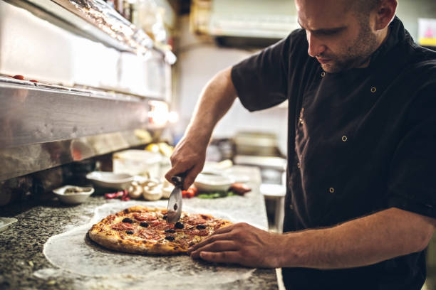 Chef Cutting Pizza Young Chef Preparing Pizza In Kitchen Restaurant pizza cutter stock pictures, royalty-free photos & images