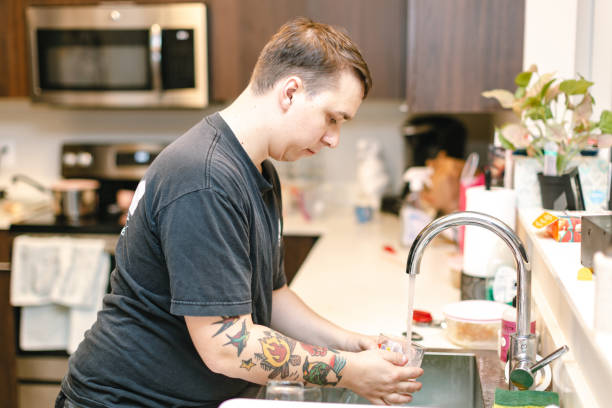 istock Young man washing dishes in apartment kitchen 1063976556