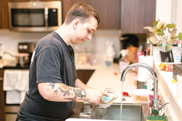 istock Young man washing dishes in apartment kitchen 1063976558