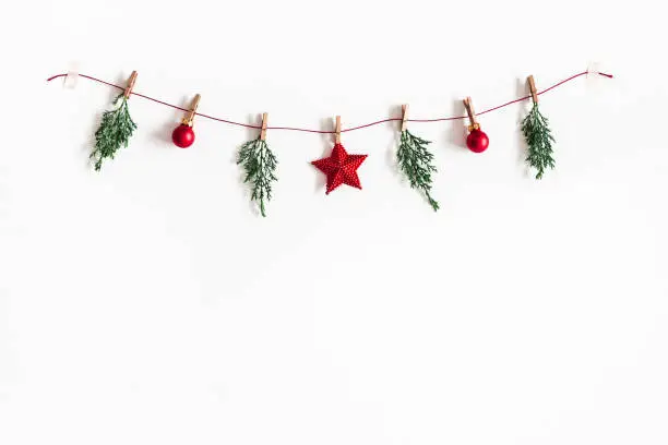 Photo of Christmas composition. Garland made of red balls and fir tree branches on white background. Christmas, winter, new year concept. Flat lay, top view, copy space