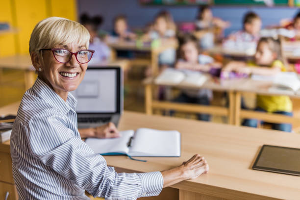 istock Happy elementary teacher at her desk in the classroom. 1064025078