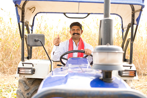 Happy farmer sitting on tractor and giving thumbs up gesture