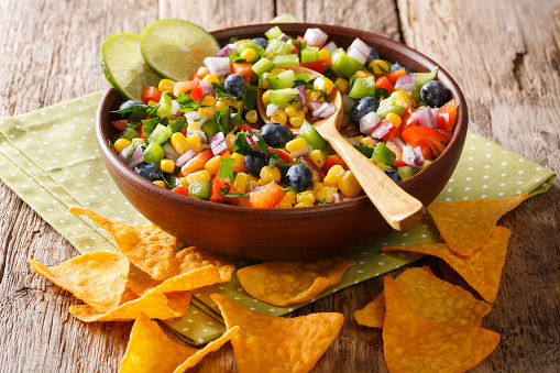 Snack a salad of corn, blueberries, peppers, herbs and onions close-up in a bowl and nachos chips on the table. horizontal
