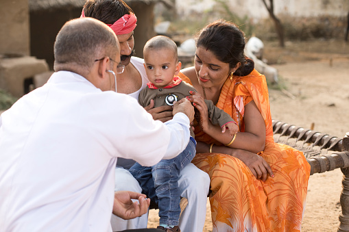 Pediatrician doctor examining ill boy during appointment at home in village