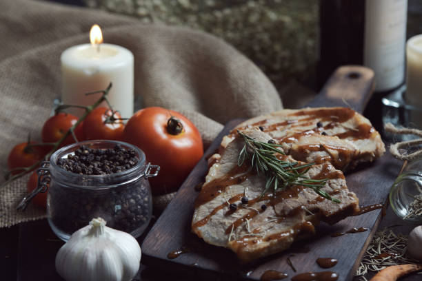 zbliżenie schabowego stek z sosem z czarnego pieprzu umieszczenie na zabytkowym drewnianym talerzu wraz z wieloma składnikami i butelka wina w ciemnym tle - pork chop fine dining wine zdjęcia i obrazy z banku zdjęć