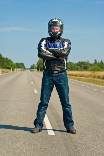 motorcyclist in helmet standing in the center of empty road