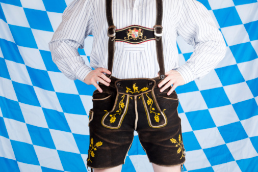 Bavarian man with black Beer Fest leather pants (Lederhose). In background is Bavarian flag visible.