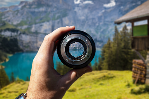 Holding camera lens in hand focus view of landscape with blue lake and bungalow