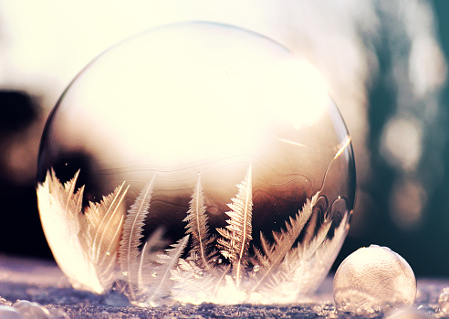 Purple frozen soap bubble ball on snow in sunset, crystal formation, winter background with copy space