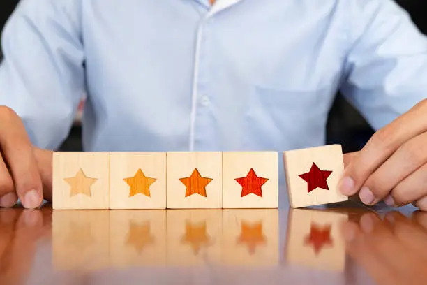 Photo of Businessman hand putting wooden five star shape on table.