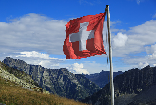 Swiss flag waving in the wind in the mountains of Ticino, Switzerland.