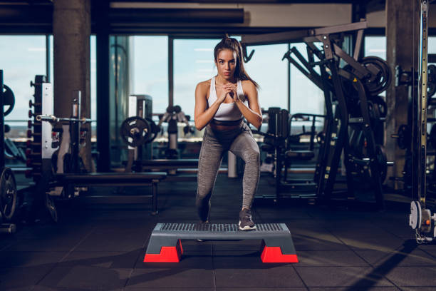 mujer joven haciendo ejercicio en equipo de gimnasia de paso en el gimnasio - subir o bajar escalones fotografías e imágenes de stock