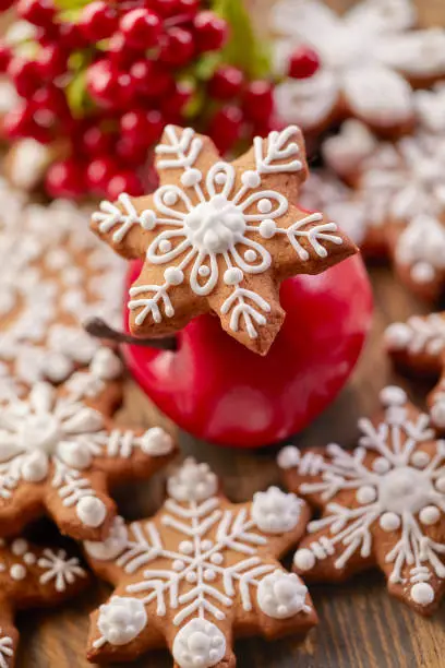 Snowflake shaped Christmas gingerbread cookie on red apple. Snowflake and star shaped cookies on wooden table