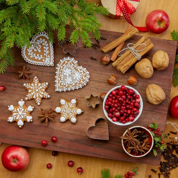 Baked Christmas gingerbread heart and snowflake shaped cookies on wooden board with cranberries, nuts, anise and cinnamon sticks. View from above
