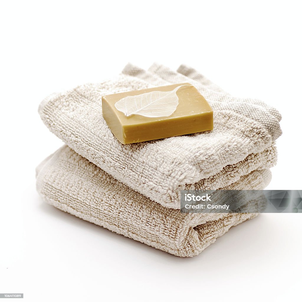 An unwrapped bar of soap atop two folded tan bath towels Bath accessories - soap and towels with skeleton leaf on white background. Bar Of Soap Stock Photo