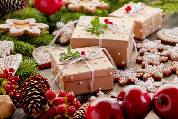 Three gift wrapped Christmas present boxes with gingerbread cookies and other festive decorations on wooden background