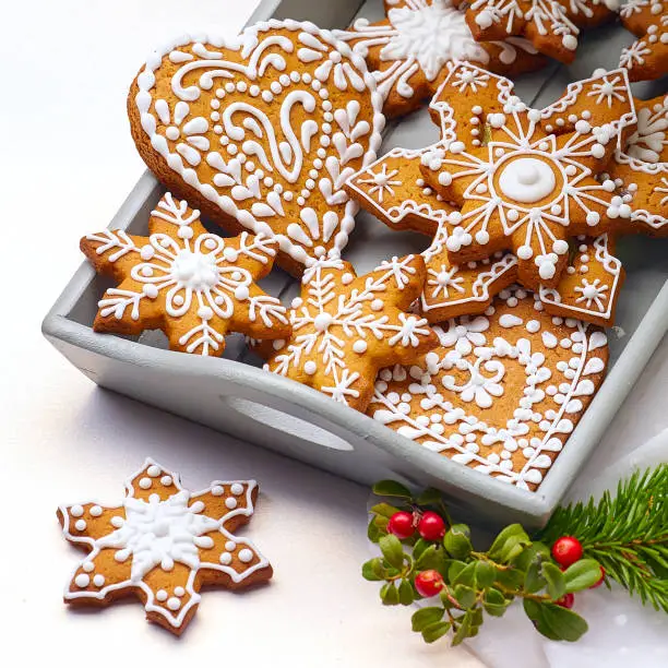 Baked and iced Christmas gingerbread cookies in light grey wooden tray