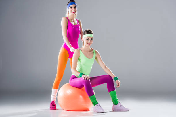 istock beautiful young sportswomen in bodysuits smiling at camera on grey 1064119266