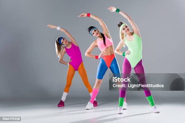 Attractive Sporty Girls In Bodysuits Training At Aerobics Workout On Grey Stock Photo - Download Image Now