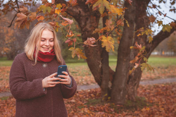 istock Smiling woman using mobile phone in park during the autumn 1064121698