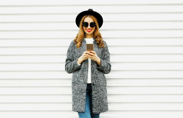 istock Fashion smiling woman using smartphone on white wall background 1064124300