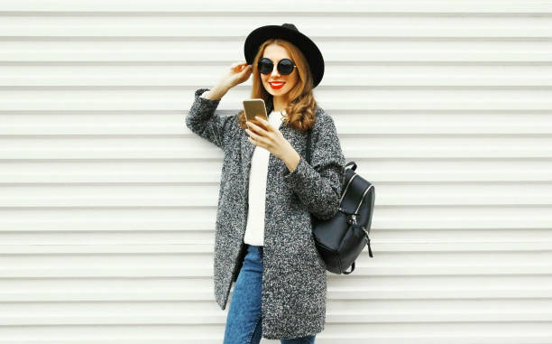 istock Fashion smiling woman using smartphone on white wall background 1064124324