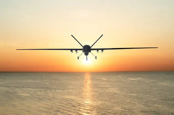 Photo of Unmanned military drone patrols the territory at sunset, flying above water surface. The view is straight ahead.