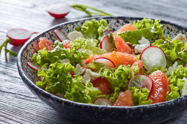 saborosa salada com ingredientes naturais - alface, fatias de rabanete, pedaços de grapefuits, queijo na bacia cerâmica sobre uma mesa de madeira cinza. - homegrown produce dairy product olive oil food - fotografias e filmes do acervo