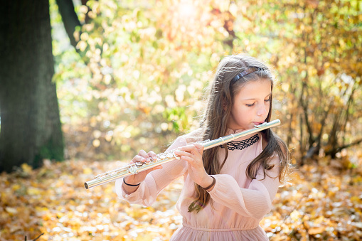 Young girl playing a flute outdoors at autumn
