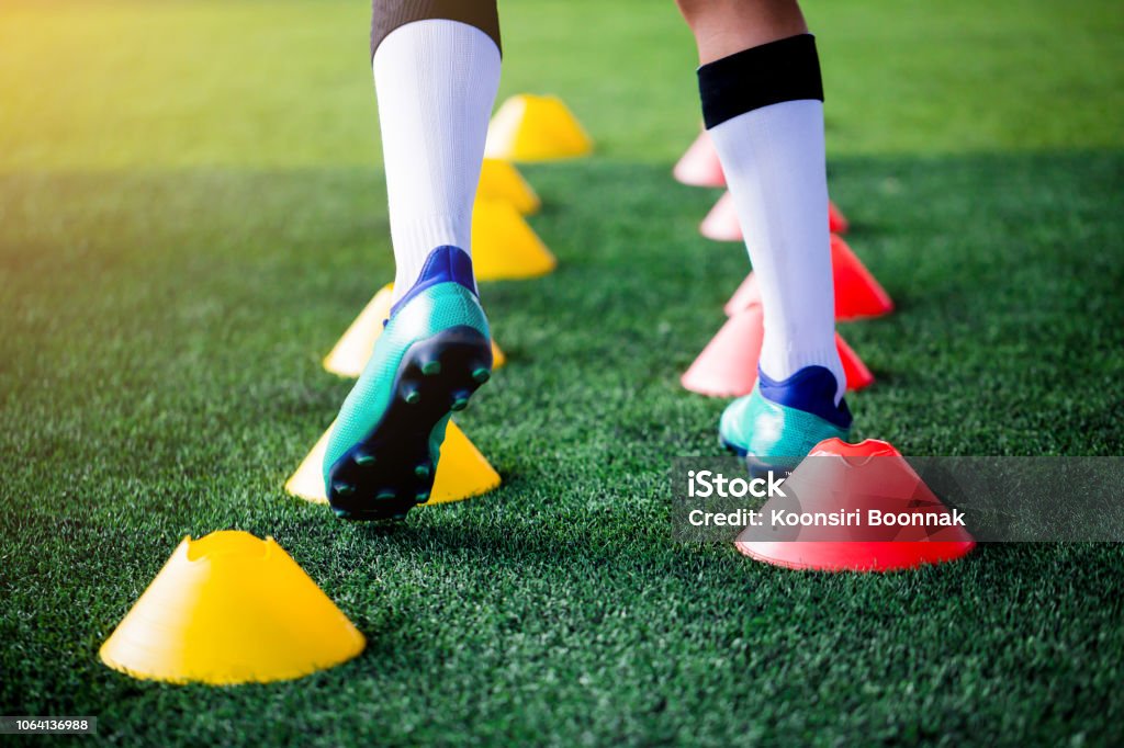 Soccer player Jogging and jump between cone markers on green artificial turf for soccer training. Soccer player Jogging and jump between cone markers on green artificial turf for soccer training. Football or Soccer Academy. Soccer Stock Photo