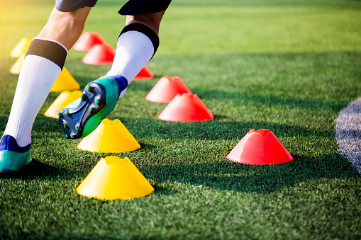 Soccer player Jogging and jump between cone markers on green artificial turf for soccer training.