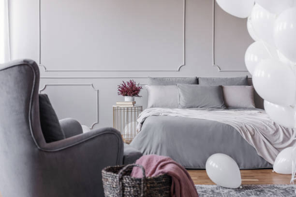 istock Trendy bedroom design with elegant double bed with grey sheets, comfortable armchair and heather on bedside table, real photo with copy space on empty grey wall 1064138418