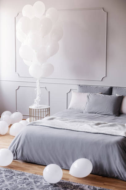 istock White balloons in stylish grey bedroom with comfortable king size bed with grey bedding and blanket, real photo with copy space on the empty wall 1064138420