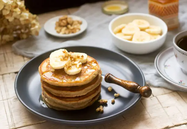Pancakes with banana, nuts and honey, served with tea. Rustic style, selective focus.