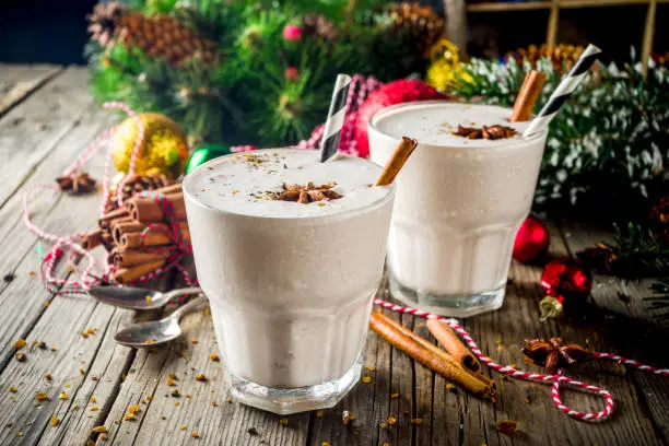 Christmas sweet cold drink, Homemade eggnog milkshake in two glasses with cinnamon and anise, old wooden background with xmas decorations copy space