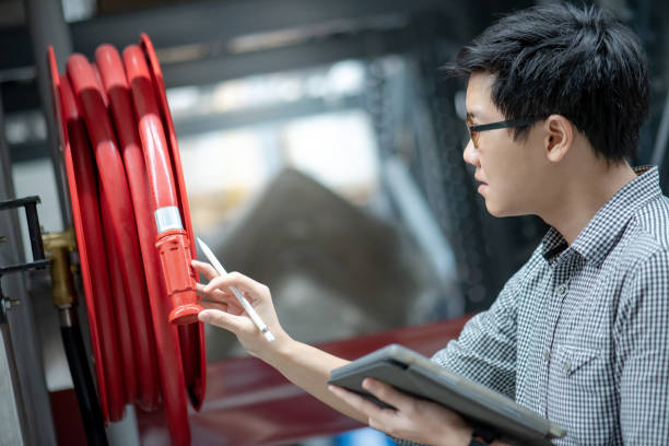 Young Asian male technician checking red fire hose reel by using digital tablet and pen. Building service and maintenance concepts Young Asian male technician checking red fire hose reel by using digital tablet and pen. Building service and maintenance concepts extinguishing photos stock pictures, royalty-free photos & images