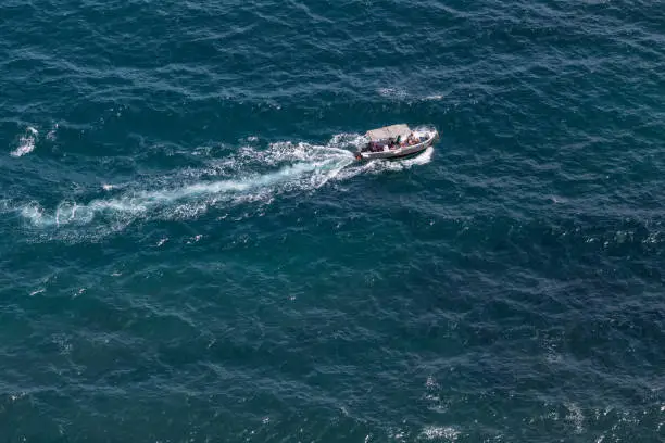 Bird's-eye-view on sea with motor boat with tent. Tour boat with seven unrecognizable persons floating at Black sea, high angle view