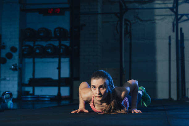 Fit woman in colourful sportswear doing burpees on a exercise mat in a grungy industrial type space stock photo
