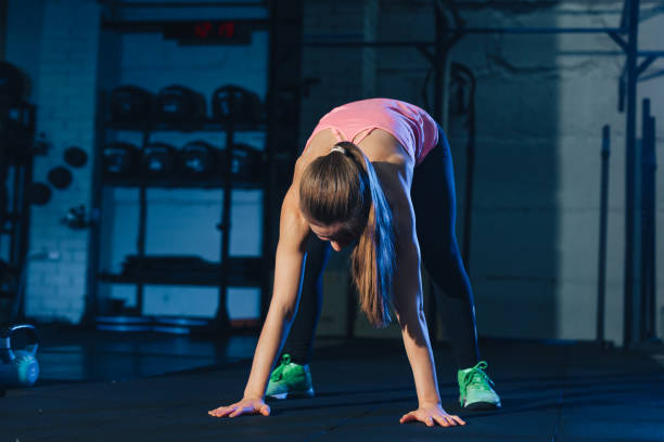 Fit woman in colourful sportswear doing burpees on a exercise mat in a grungy industrial type space stock photo
