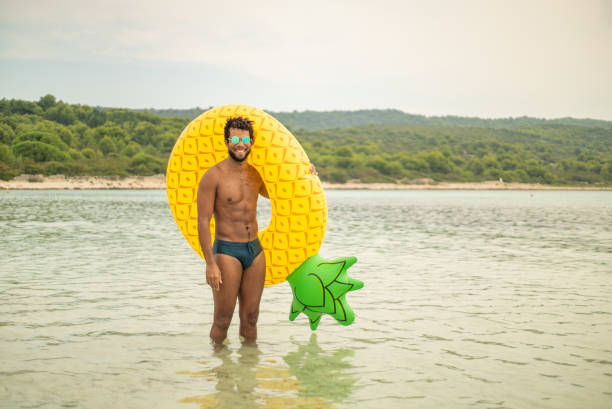 vista aérea de homem com colchão inflável abacaxi em forma, sorrindo. - calções de corrida - fotografias e filmes do acervo