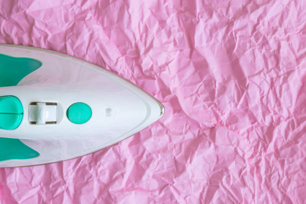 Top view of iron against pastel pink wrinkled paper minimal creative concept. Space for copy.