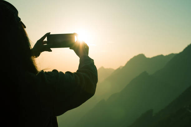 istock Woman photographing mountain sunset using mobile phone 1064164152