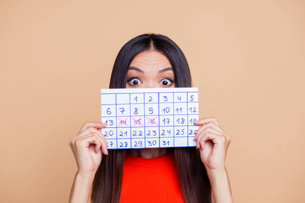 nahaufnahme foto portrait of erschrocken überrascht mit großen augen dame schließen abdeckung sie gesicht mit handgefertigten kalender aus papier isoliert auf pastell beige hintergrund textfreiraum - stilrichtung des stock-fotos und bilder