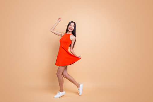 Full length size studio photo portrait of beautiful charming good mood toothy beaming smile tender careless carefree cheerful gorgeous korean teen lady holding skirt isolated pastel beige background