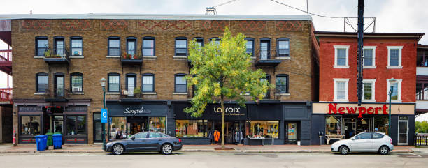 Magog Quebec Canada Rue Principale brick apartment building with stores panoramic view Panoramic view of a Magog Quebec Canada Rue Principale brick apartment building with stores in the historical downtown district with flowers in the foreground. Cars are parked; recycling bins on the sidewalk. lake magog photos stock pictures, royalty-free photos & images