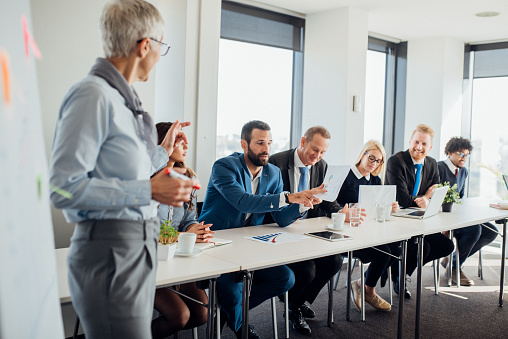 Woman secretary using laptop and discussing job with her employer, middle aged man, during meeting in conference room.